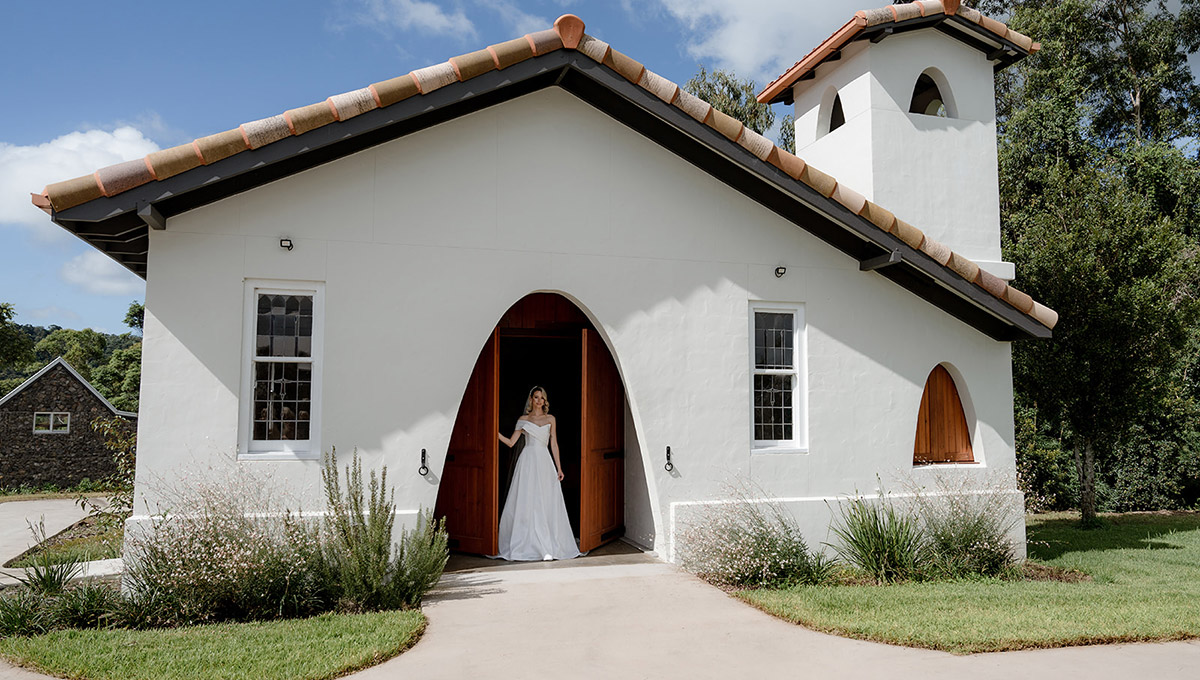 A bride in a classic Erin Clare Bridal gown standing in the doorway of a white-washed chapel, embodying the perfect blend of classic elegance and modern charm at Goodwater Ridge.
